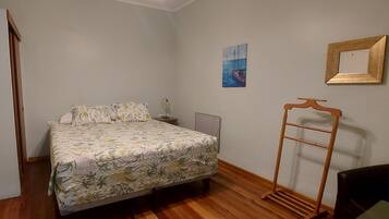 A bedroom with a bed, a nightstand, a lamp, a wooden chair, a wooden ladder, and a framed picture on the wall.