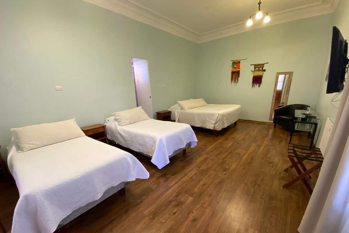Una habitación con tres camas individuales, suelo de madera, un escritorio con silla y televisión.