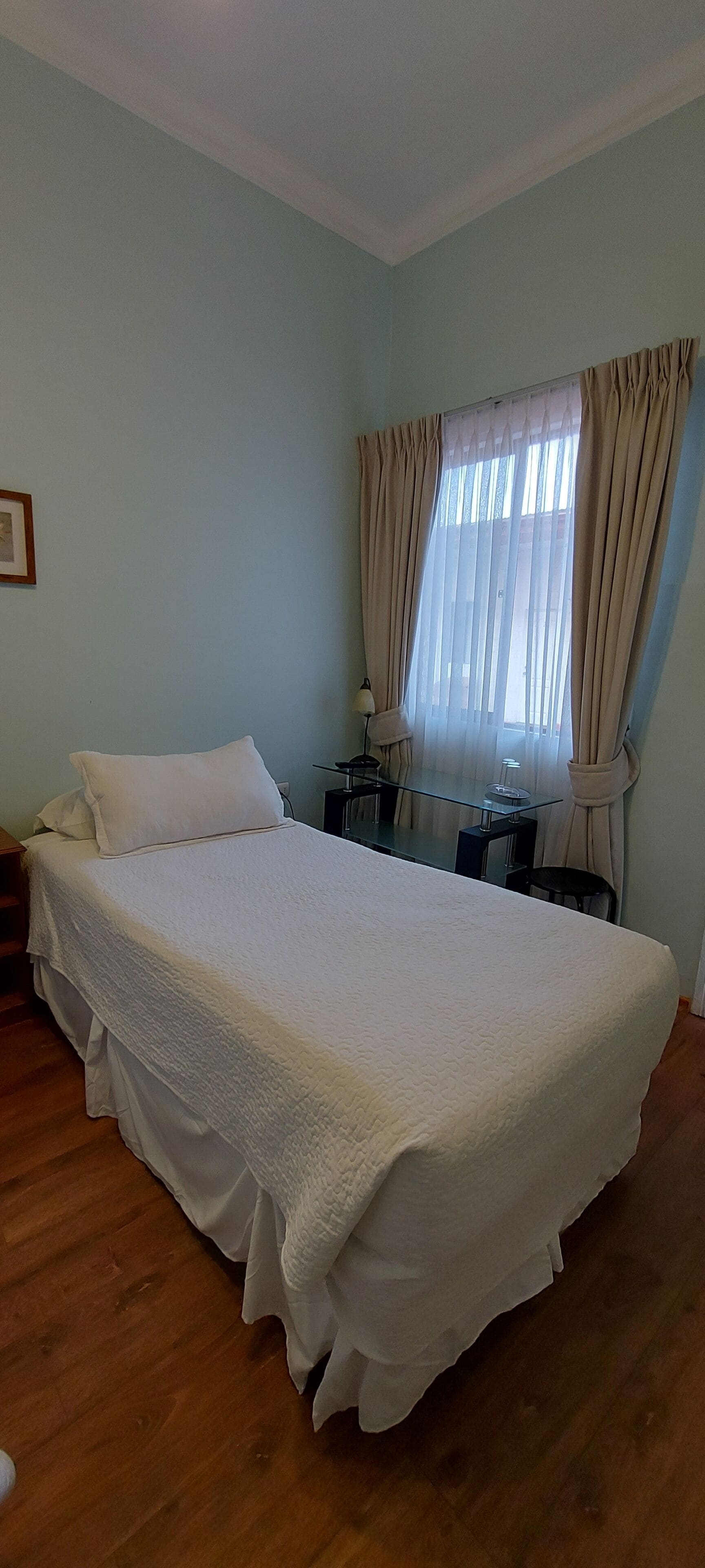 A bedroom with a large bed, a small table, a chair, and a window with curtains.