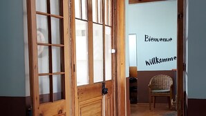 Una puerta de madera con paneles de vidrio que da a una habitación con un tapete de piso a cuadros y una silla de mimbre.