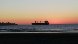 Un carguero silueteado contra un atardecer en el océano.