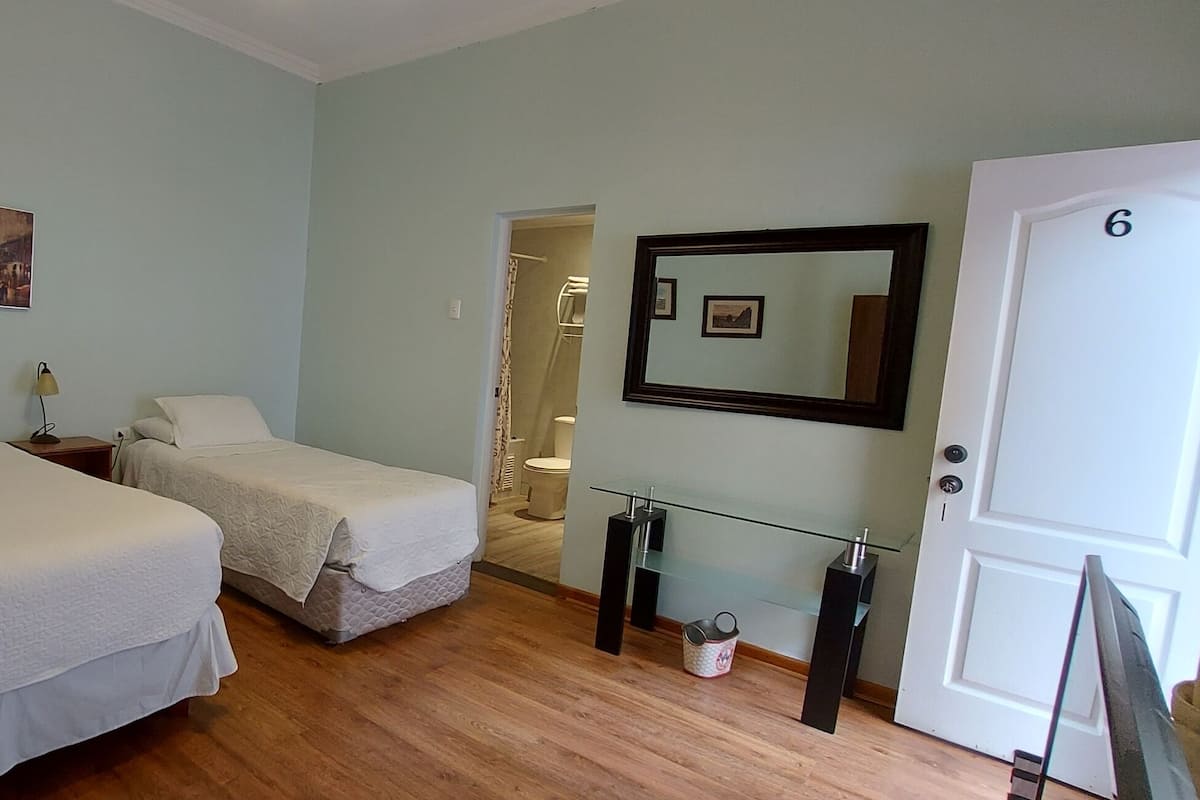 Una habitación con dos camas, una mesita de noche con lámpara, un espejo y una puerta con el número 6.