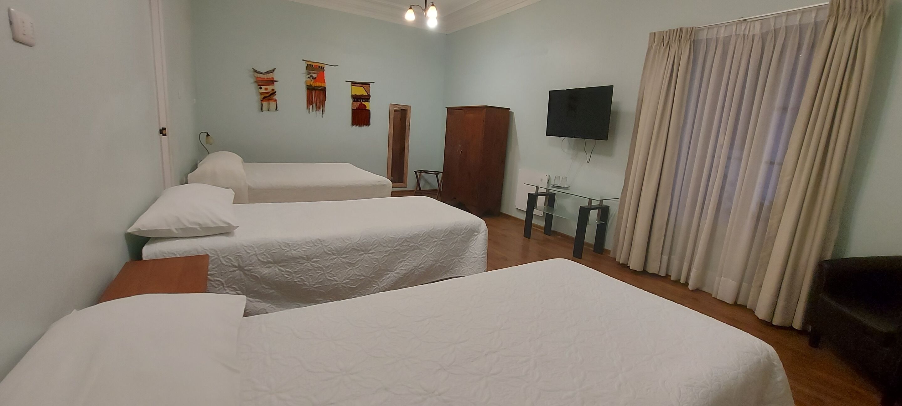 A hotel room with two beds, a TV, a wooden wardrobe, and a glass table.