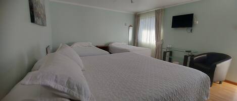 A hotel room with a large bed, a TV mounted on the wall, and a chair.