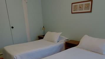 Una habitación con dos camas, piso de madera, una puerta blanca y una lámpara en el techo.