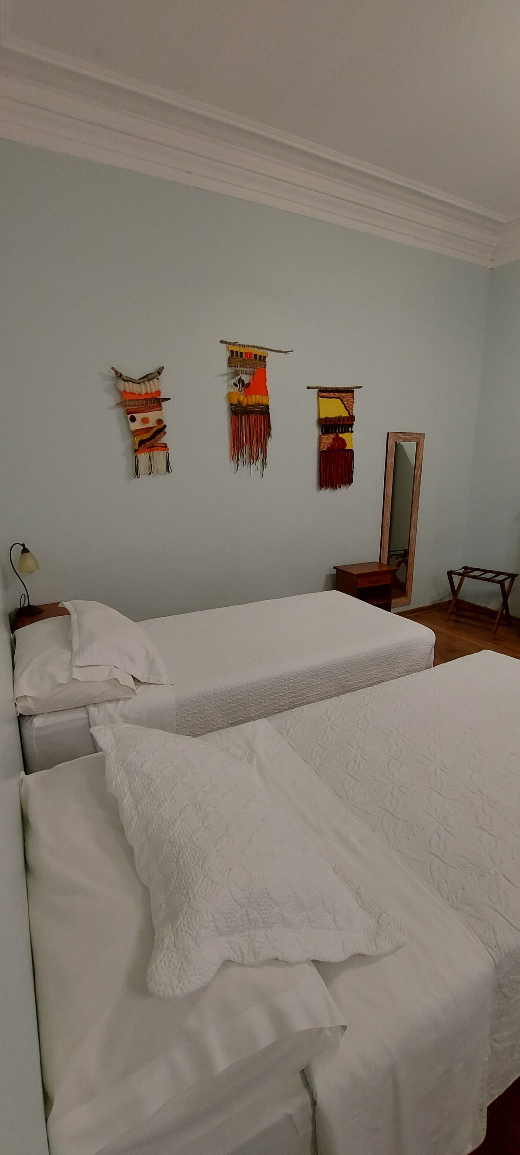 A room with two beds, a mirror, and wall hangings.