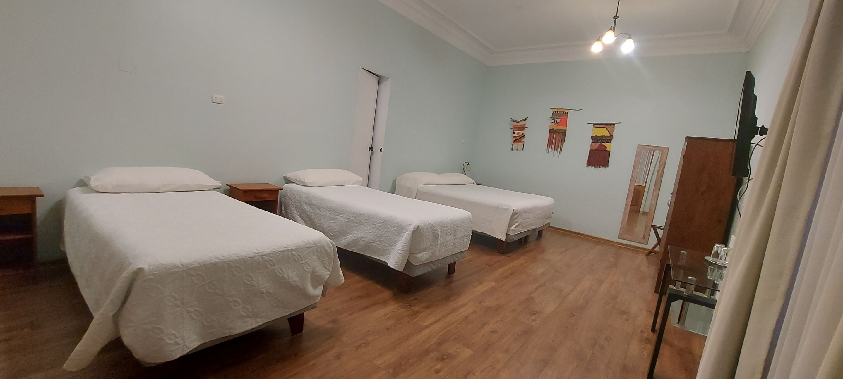 A hotel room with three beds, wooden flooring, a door, and wall decorations.
