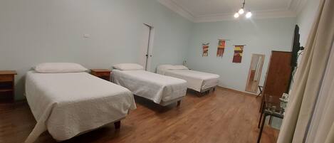 A hotel room with three beds, wooden flooring, a door, and wall decorations.