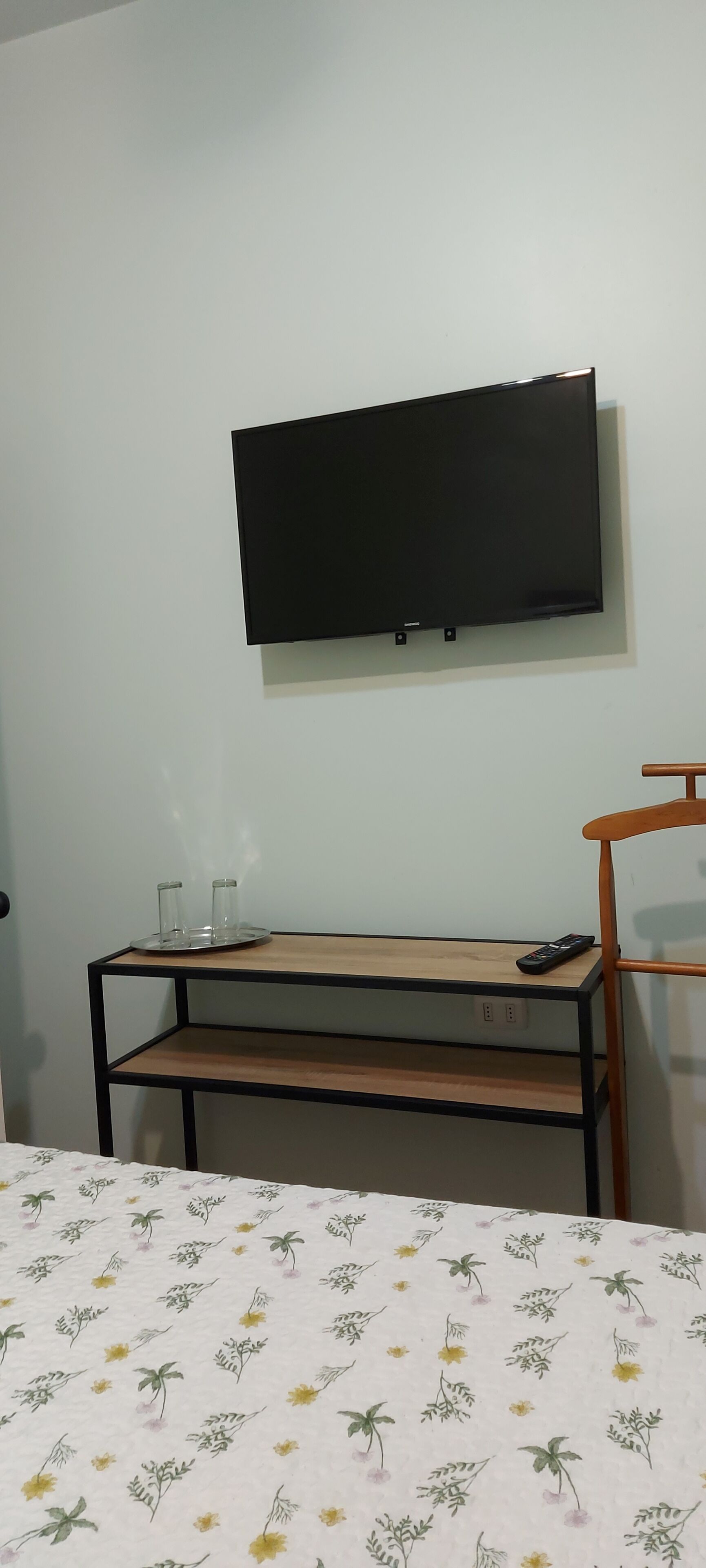 Une chambre avec un lit, un téléviseur fixé au mur, une petite table avec un plateau et des verres, et une chaise.