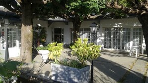 A courtyard with a white building, outdoor seating, and a tree. - Le Malatras (Tullins)