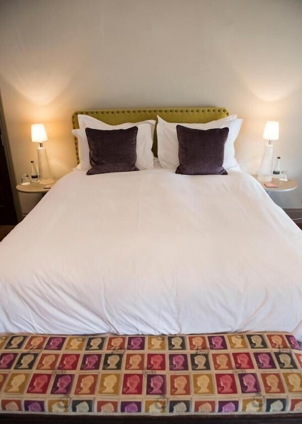A neatly made bed with white linens, two dark pillows, and a colorful headboard. - The Priory (Leyburn)