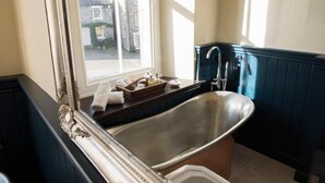 A bathroom with a large, ornate mirror, a freestanding bathtub, and a window with a view of a street. - The Priory (Leyburn)
