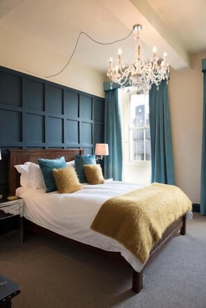 A bedroom with a large bed, a chandelier, and a view of the city through a window.