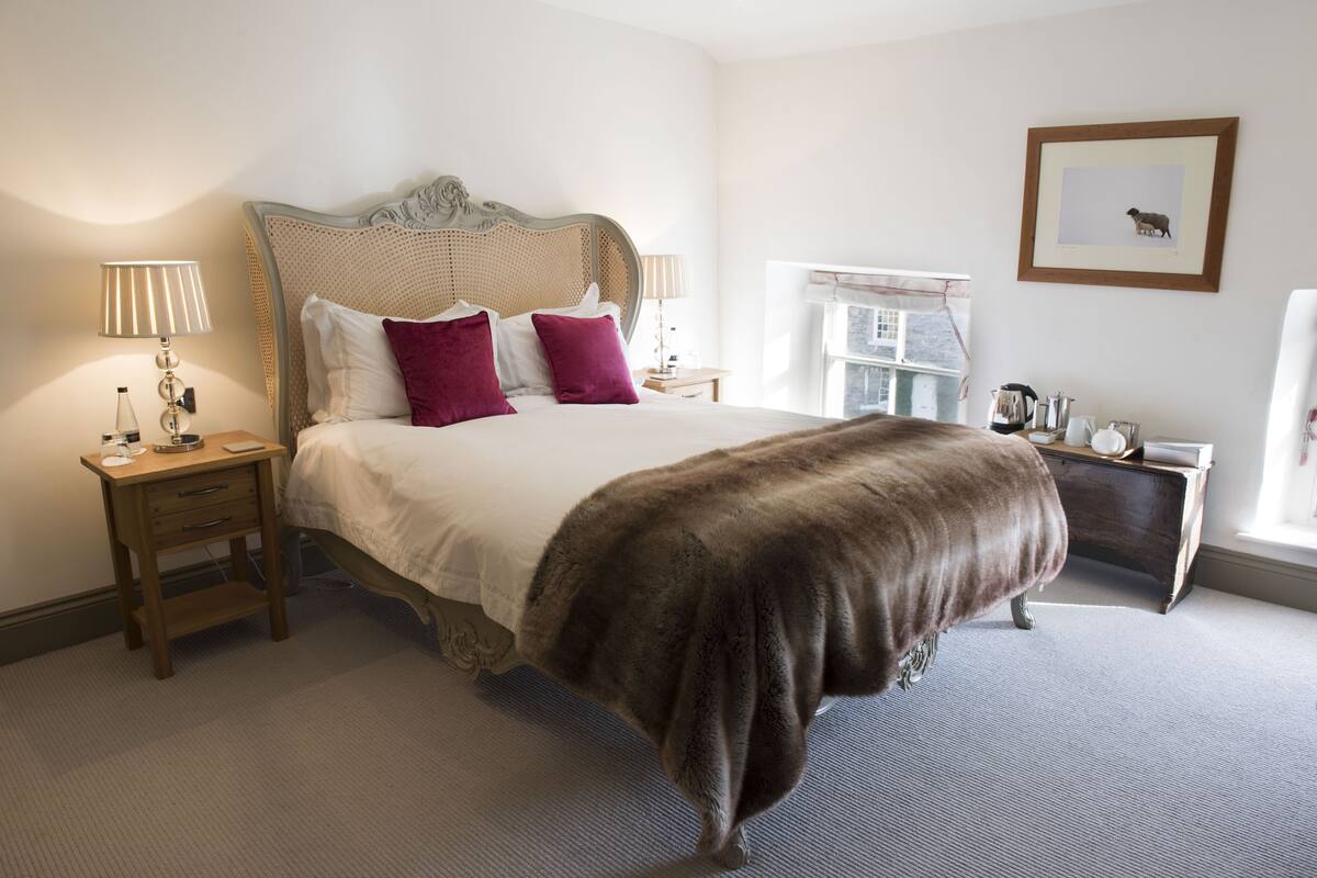 A neatly arranged bedroom with a large bed, two bedside tables, a nightstand, a dresser, and a framed picture on the wall.