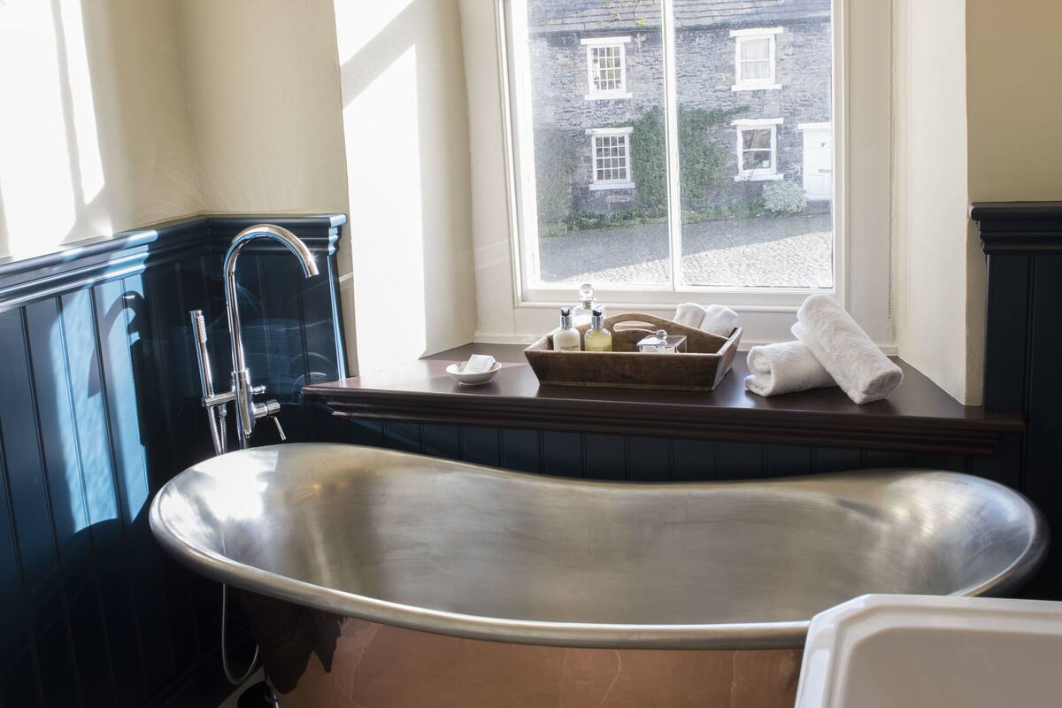 A bathroom with a freestanding bathtub, a window with a view of buildings, and a wooden tray with toiletries.