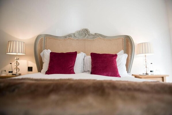 A bed with a woven headboard, two red pillows, and two bedside lamps.