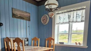 Ein Esszimmer mit Holztisch und -stühlen, einer Hängelampe, einer Uhr und einem Fenster mit Blick ins Freie.