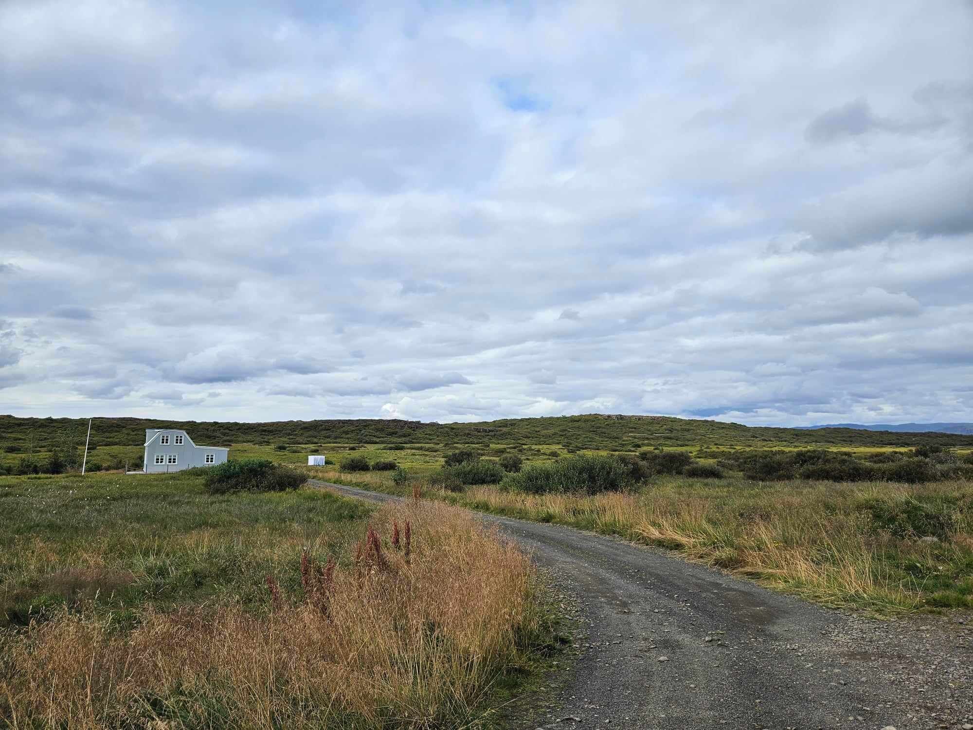 Un paisaje rural con un camino de tierra que lleva a un edificio blanco.