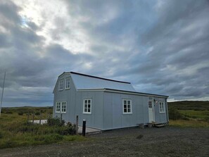 A small, single-story building with a metal roof, white trim, and a wooden deck.