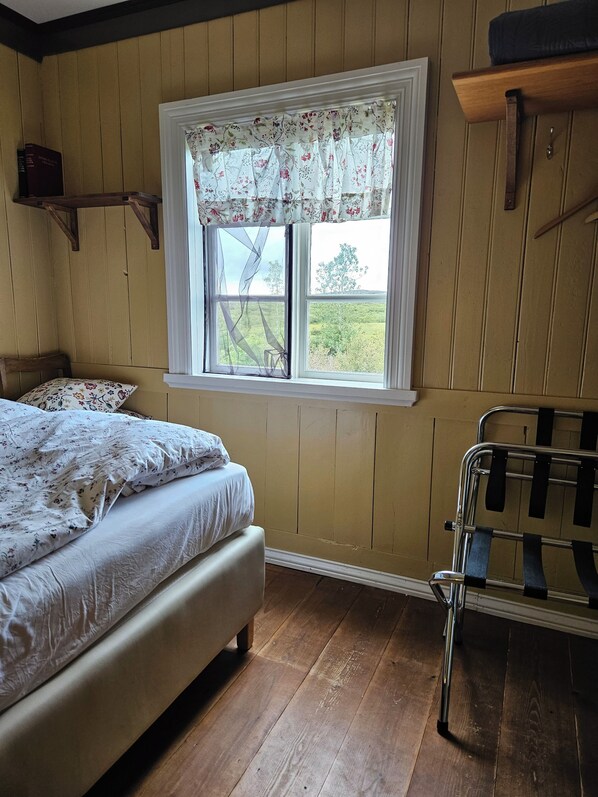 A bedroom with a wooden floor, a bed with floral bedding, a window with floral curtains, and a metal rack.