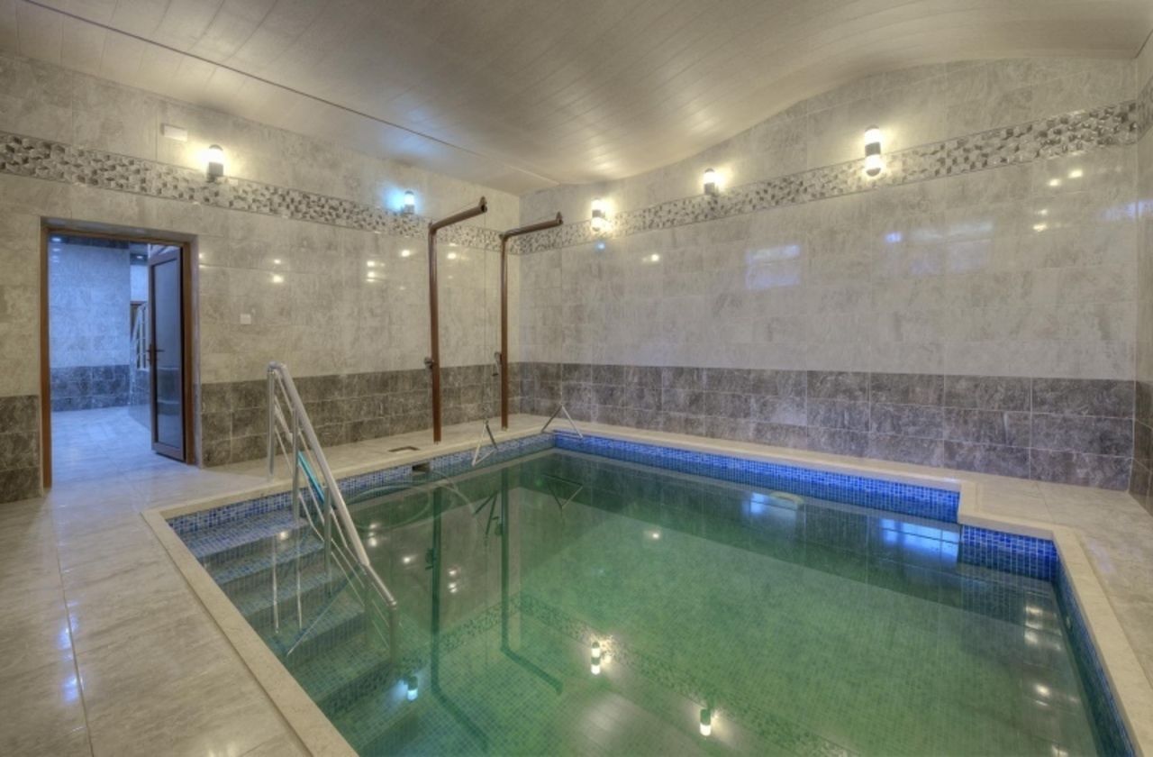 An indoor swimming pool with clear water, a tiled floor, and a stone wall with a blue border.