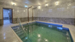 Una piscina interior amb aigua cristal·lina, un terra solat i una paret de pedra amb una franja blava.