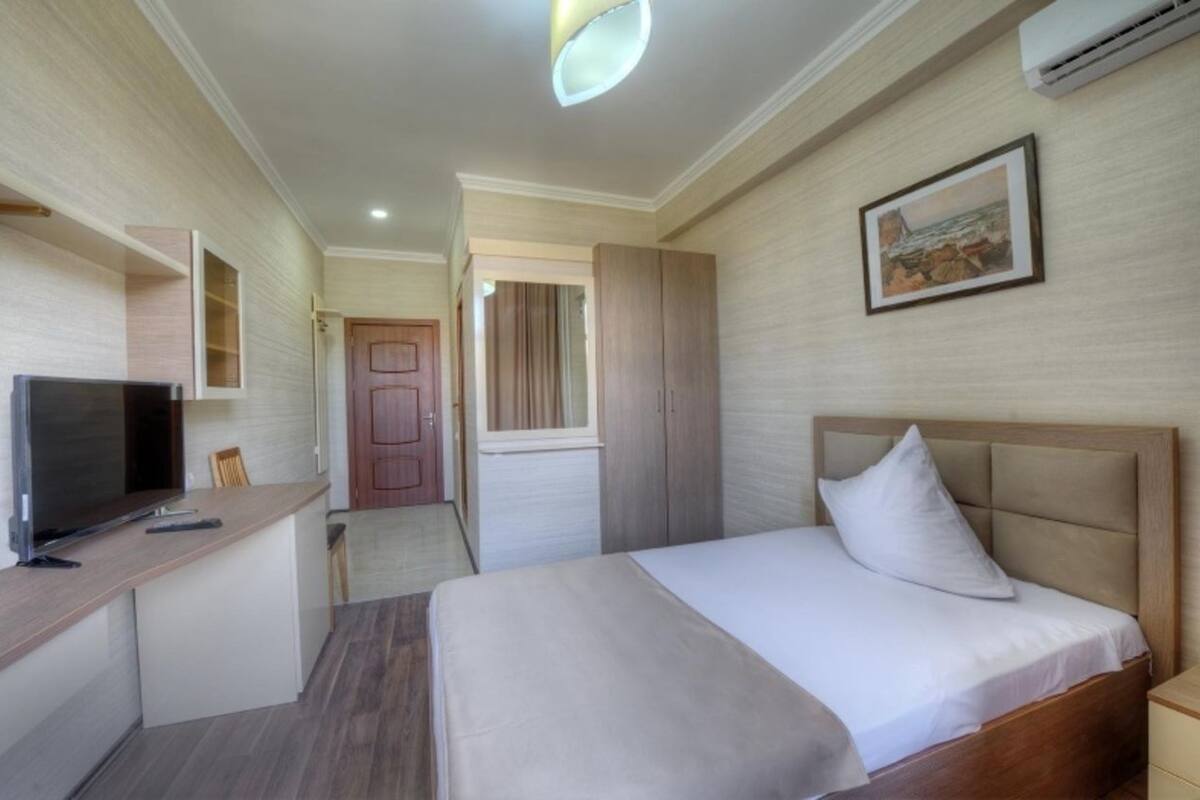 Une chambre d’hôtel avec un lit, un bureau avec une télévision, une armoire et un tableau au mur.