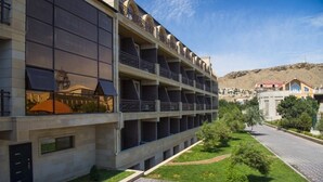 Un edifici modern amb nombroses balcons, un pati empedrat i una vista d'un paisatge amb muntanyes al fons.