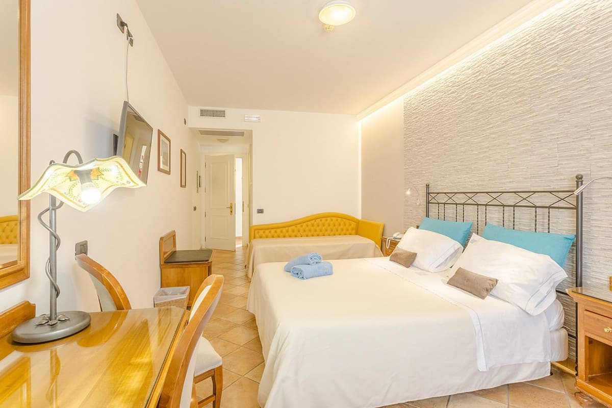 A hotel room with two beds, a desk, a lamp, and a bathroom visible in the background.