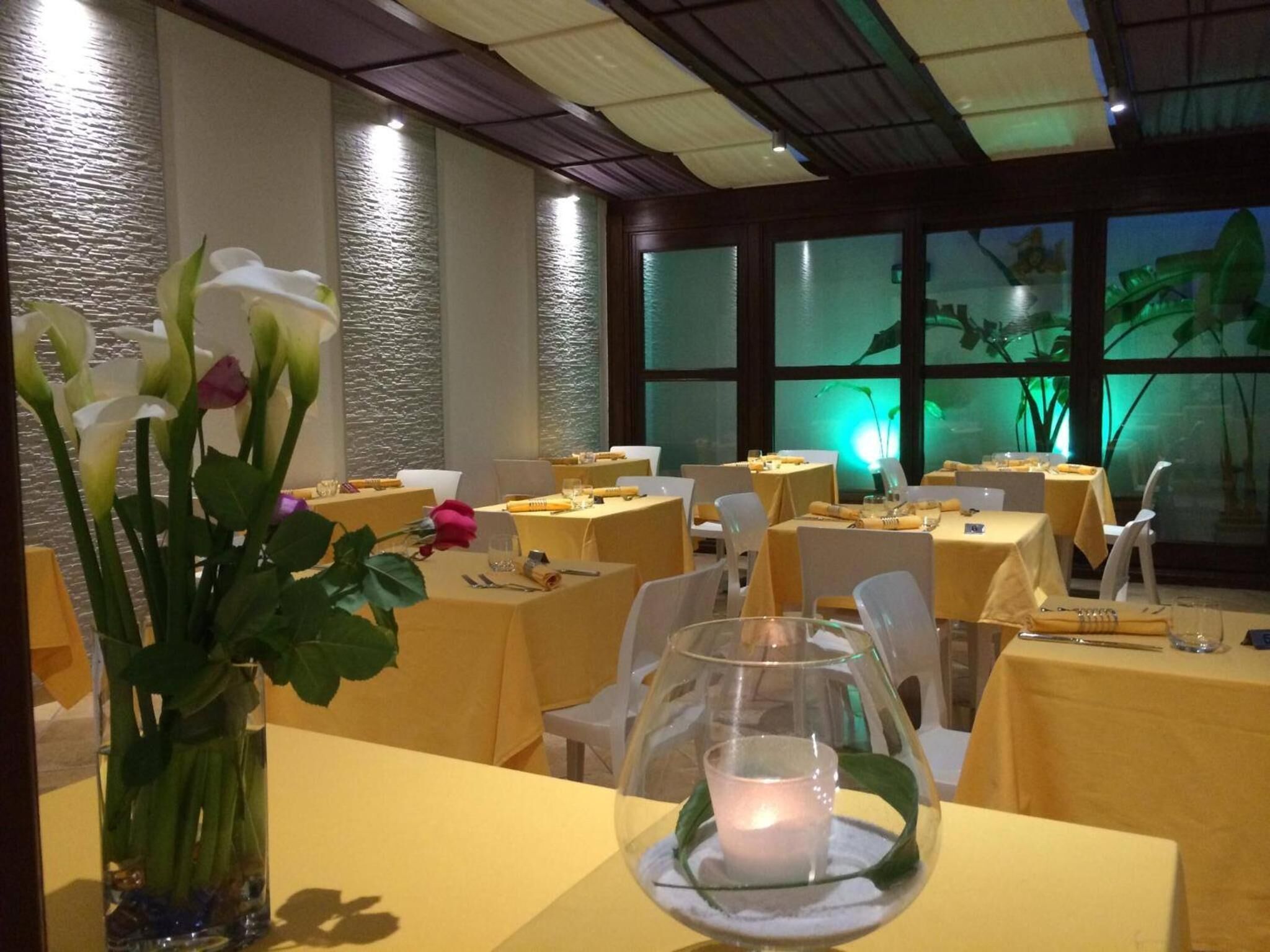 A restaurant with tables set for dining, a vase with flowers, and a candle on the table.