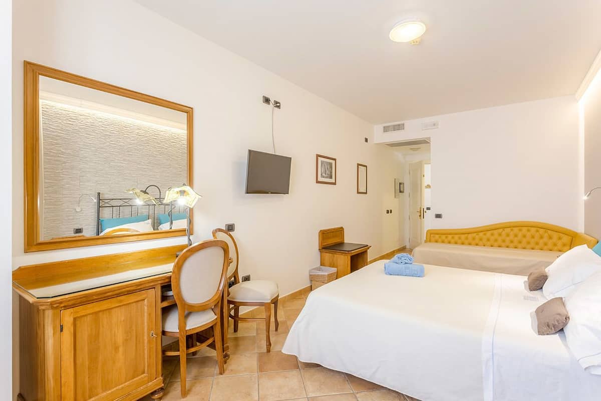 A hotel room with a bed, a desk with a chair, a television, and a large mirror.