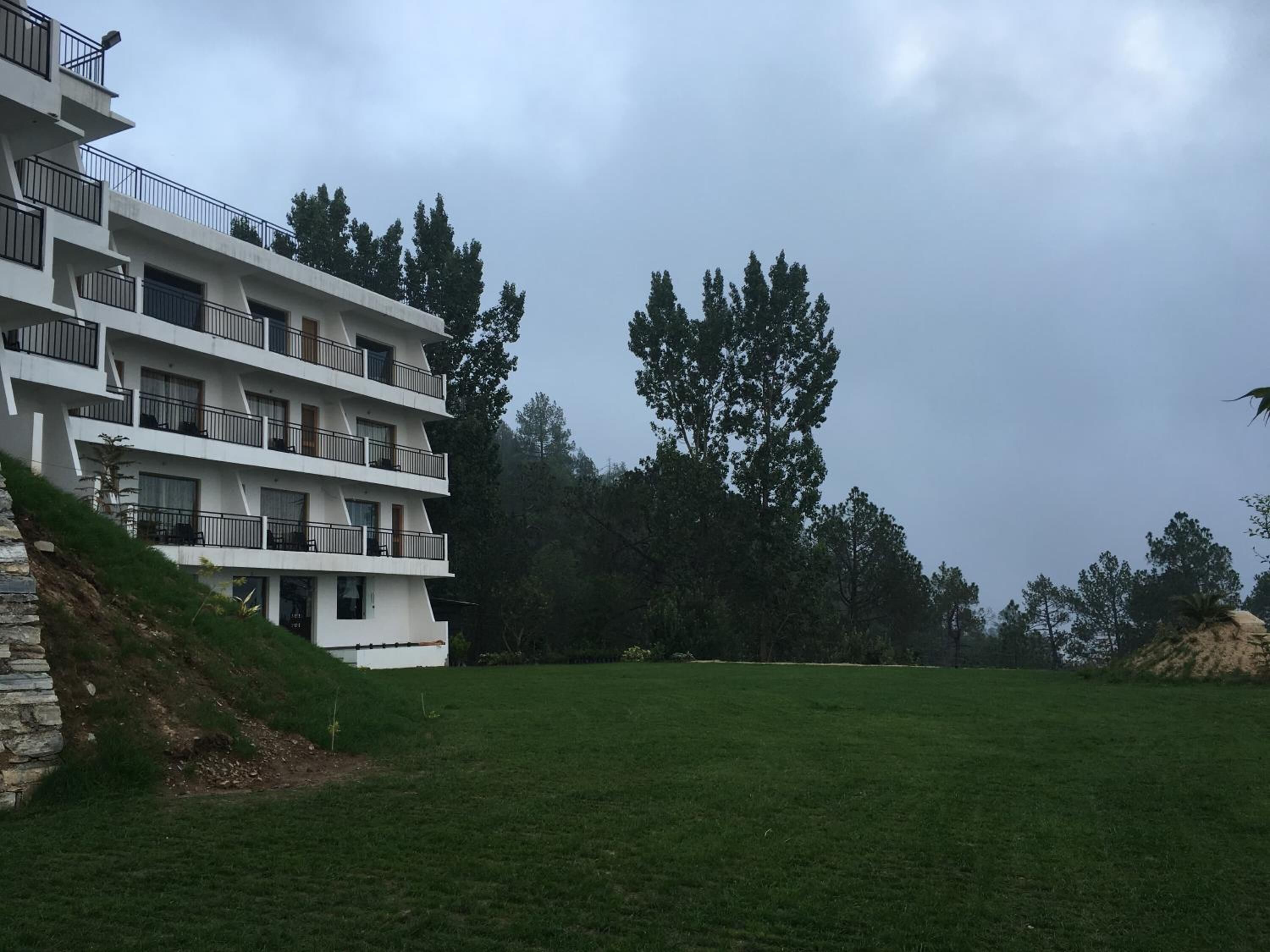 Un edificio de varios pisos con balcones, rodeado de césped y árboles.