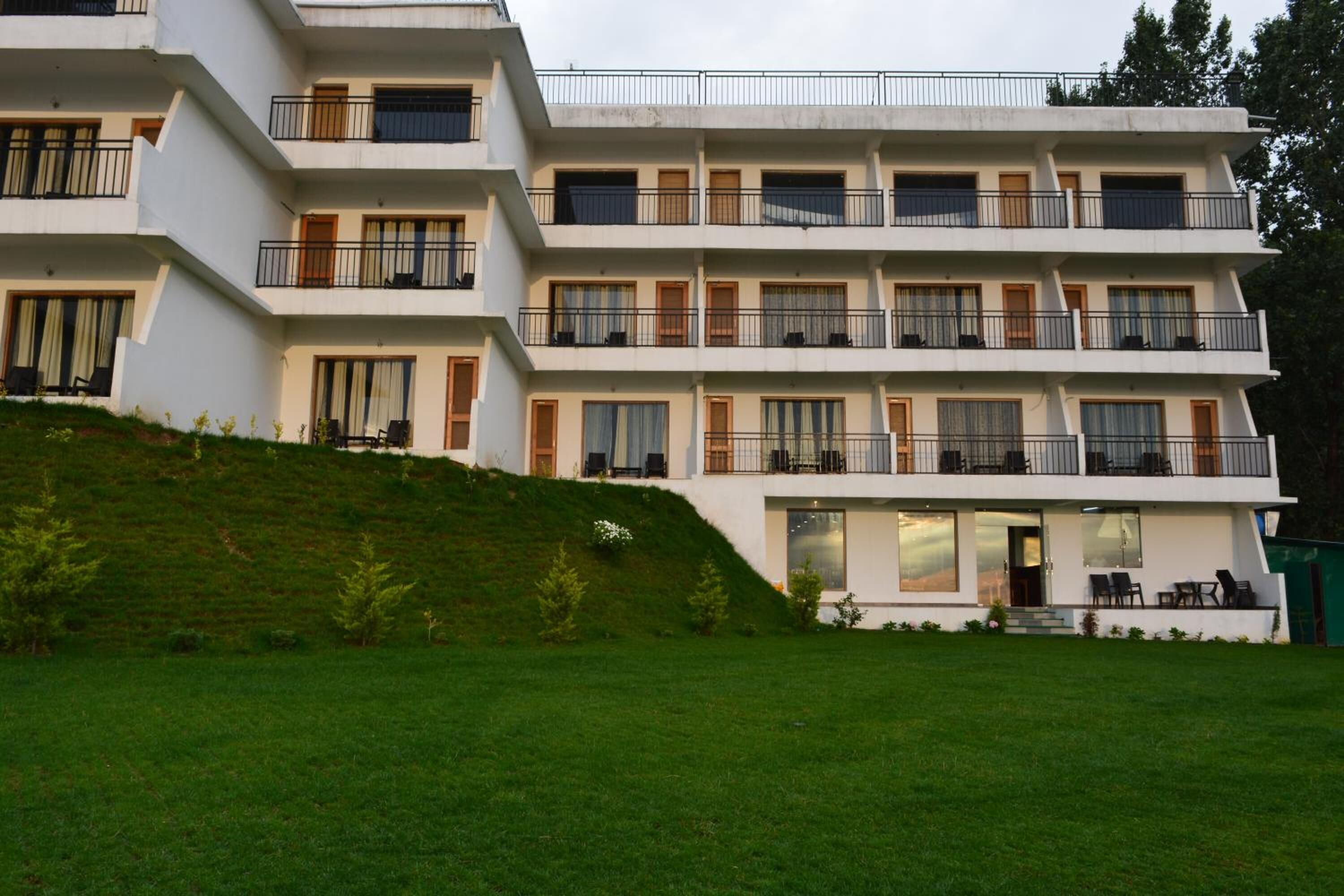 Een meerlaags hotel met balkons, grote ramen en een grashelling.