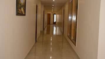 A long, well-lit hallway with a tiled floor, doors on both sides, and a framed picture on the left wall.