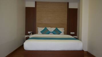 Una habitación de hotel moderna con cabecera de madera, una cama grande con ropa blanca y almohadas turquesa, y piso de madera.