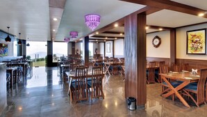 Un restaurante espacioso con mesas y sillas de madera, ventanas amplias y un candelabro.