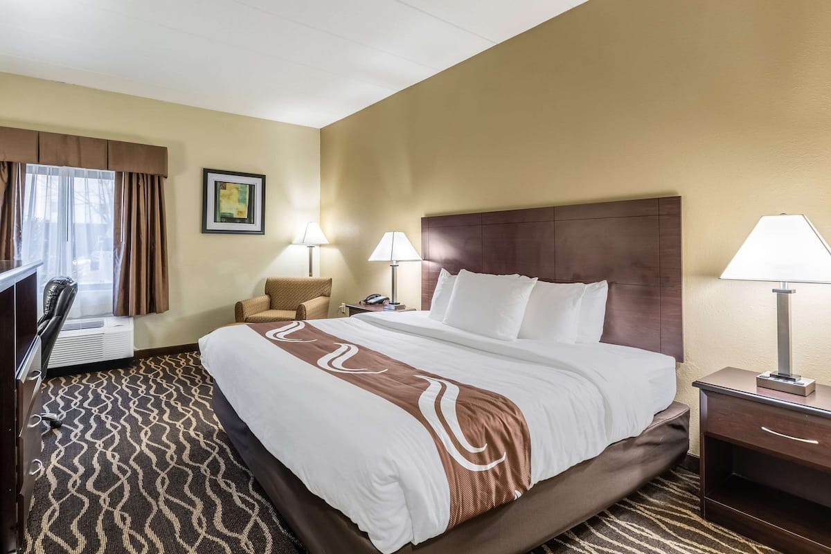 A hotel room with a large bed, two bedside lamps, a chair, a desk, and a window with curtains.