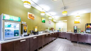 A self-service breakfast area with a coffee machine, a refrigerated display case, and a variety of food items on the counter. - Quality Inn & Suites Southport (Indianapolis)