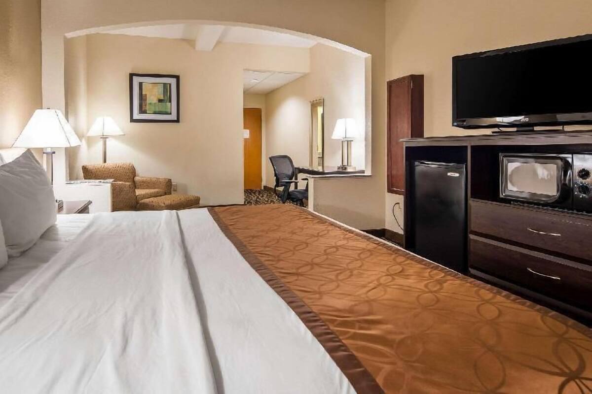 A hotel room with a bed, a desk with a chair, a television, and a refrigerator.