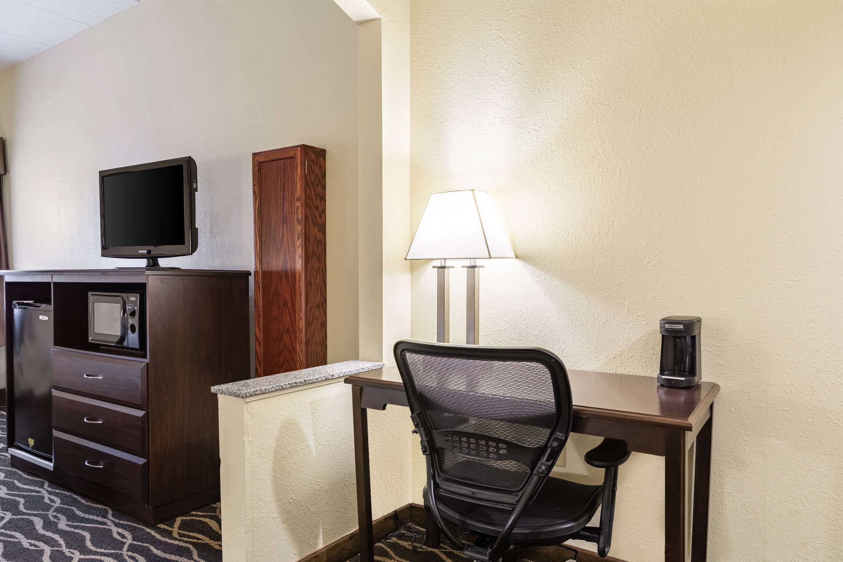 A hotel room with a desk, a chair, a television, a lamp, and a coffee maker.