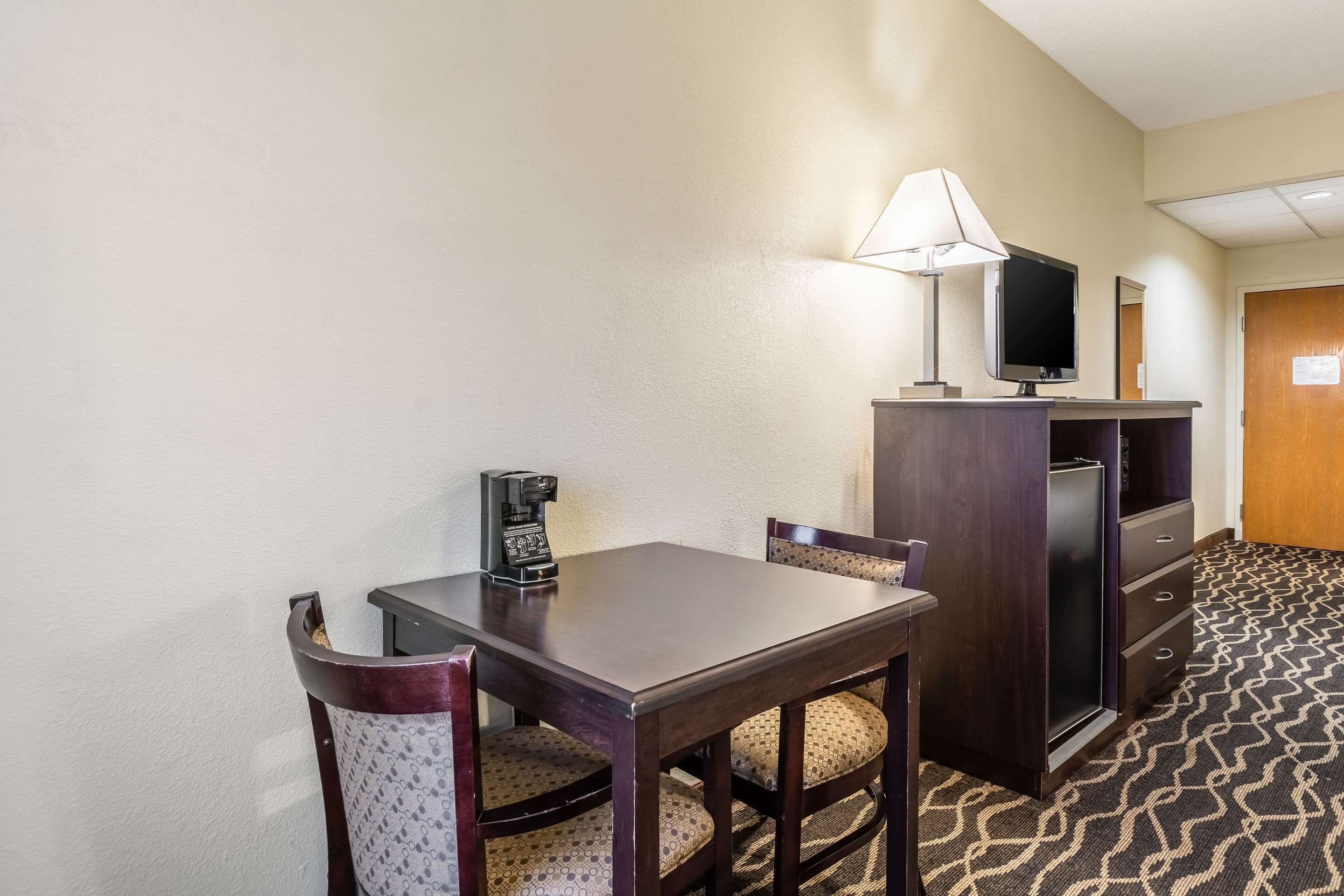 Une chambre d’hôtel équipée d’un bureau en bois, d’une chaise, d’une télévision, d’une lampe et d’un mini-bar.