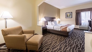 A hotel room with a bed, two bedside tables with lamps, a chair, and a patterned carpet. - Quality Inn & Suites Southport (Indianapolis)