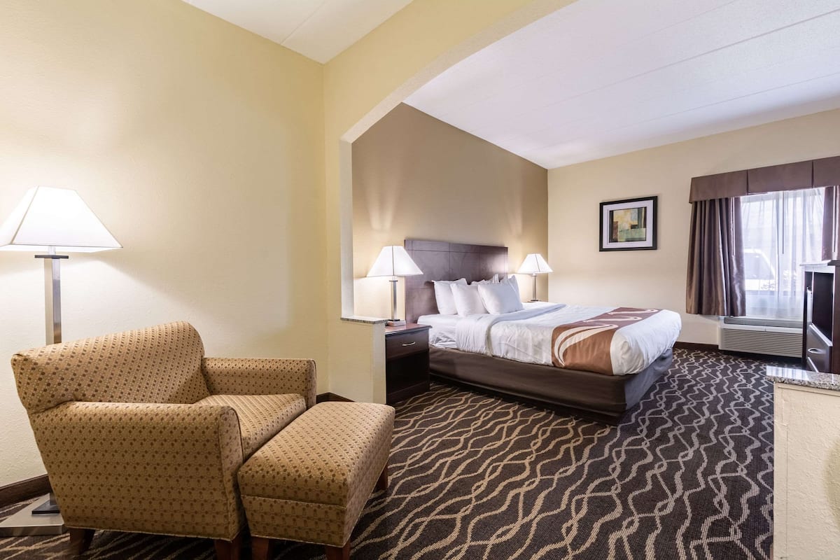 A hotel room with a bed, two bedside tables with lamps, a chair, and a patterned carpet.