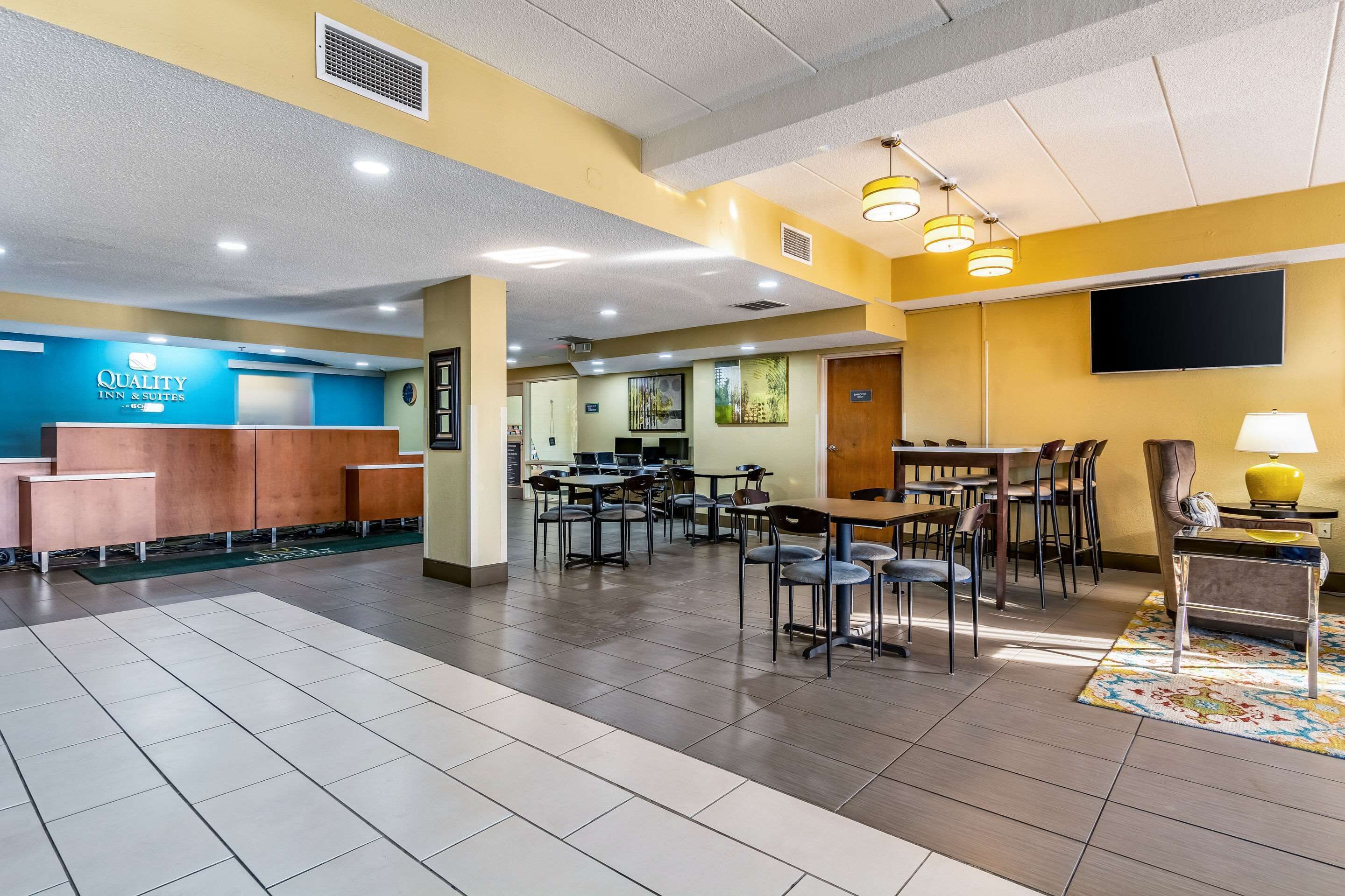 A hotel lobby with a reception desk, multiple tables and chairs, and a television mounted on the wall.