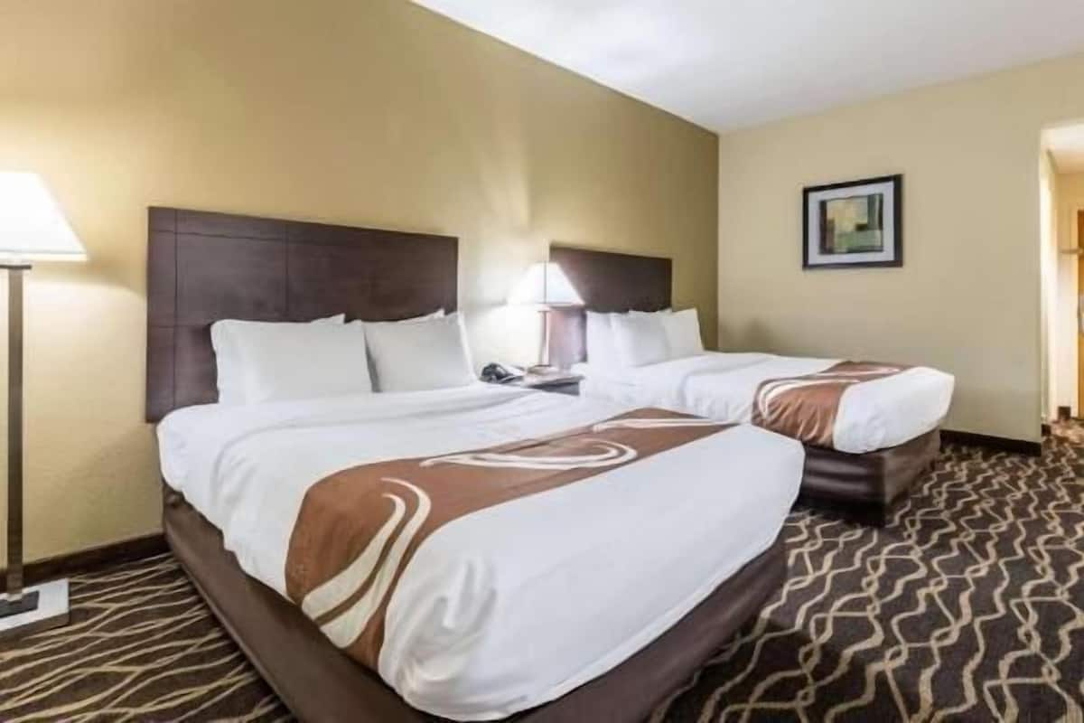 A hotel room with two beds, a headboard, a nightstand, a lamp, and a framed picture on the wall.
