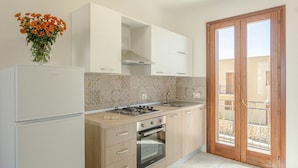 Eine Küche mit Gasherd, Backofen und Spüle. Es gibt einen Holzschrank und einen weißen Kühlschrank.