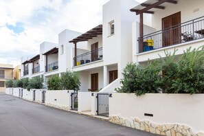 Una hilera de modernas casas adosadas de dos plantas, con balcones, paredes de piedra y una calle pavimentada.