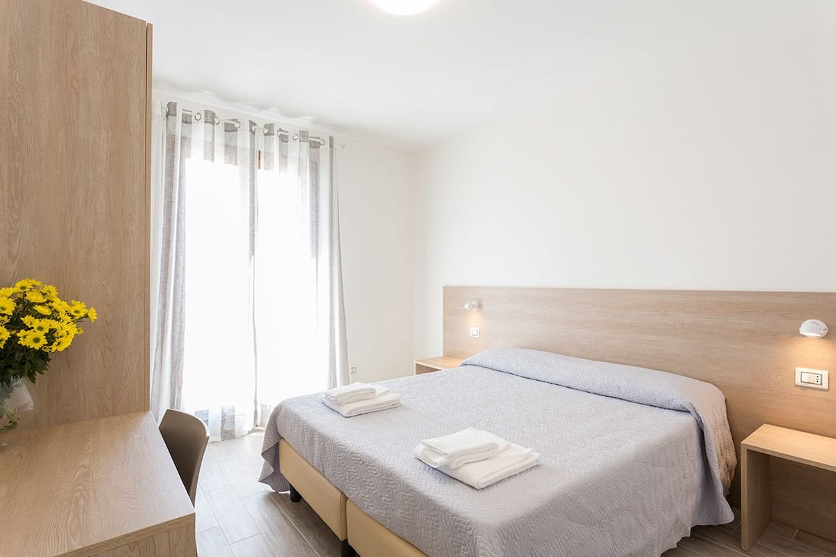 Een hotelkamer met een bed, nachtkastjes, een bureau en een raam met gordijnen.
