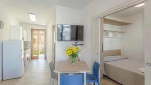 Ein kompakter Raum mit Küchenzeile, einer Essecke mit Tisch und Stühlen, einem Bett und einem an der Wand befestigten Fernseher.