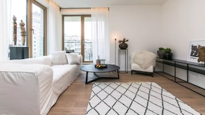 A modern living room with a white sofa, a round coffee table, and a patterned rug. - Flawless Apartments Pod Děkankou (Prague)